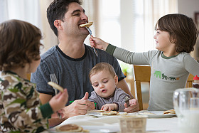 Adult with 2 children and 1 baby at family table consuming food.